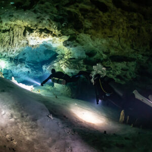 Two cave divers on a pale sandy floor with torch pools of light, Quintana Roo, Mexico