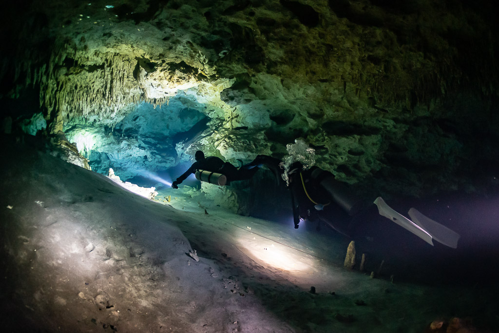 Two cave divers on a pale sandy floor with torch pools of light, Quintana Roo, Mexico