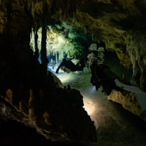 Two divers squeezing past stalagmites in a narrow cave passage, Quintana Roo, Mexico