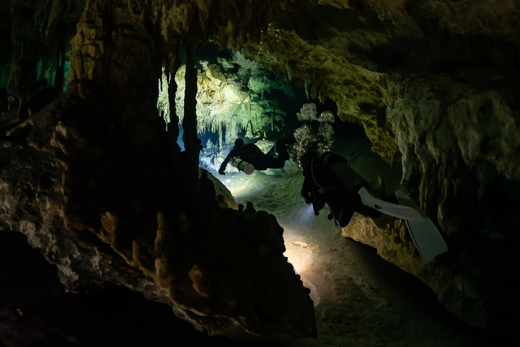 Two divers squeezing past stalagmites in a narrow cave passage, Quintana Roo, Mexico