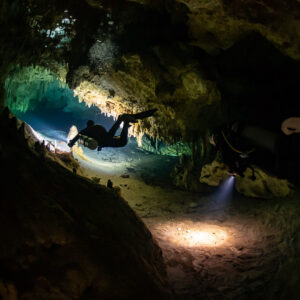 Two divers in a low cave tunnel, one lighting the floor, Quintana Roo, Mexico