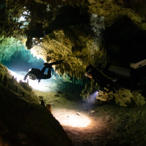 Two divers in a low cave tunnel with bubbles rising to the ceiling, Quintana Roo, Mexico