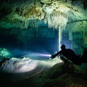 Sidemount diver in silhouette lighting a stalactite-hung cave room, Quintana Roo, Mexico