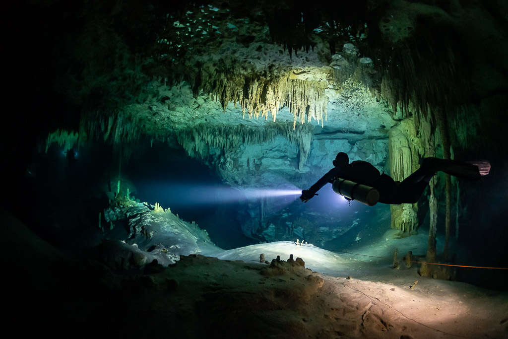 Sidemount diver lighting a cave room with stalactites and white floor, Quintana Roo, Mexico