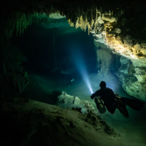 Diver with torch below a high stalactite ceiling in a dark cave, Quintana Roo, Mexico