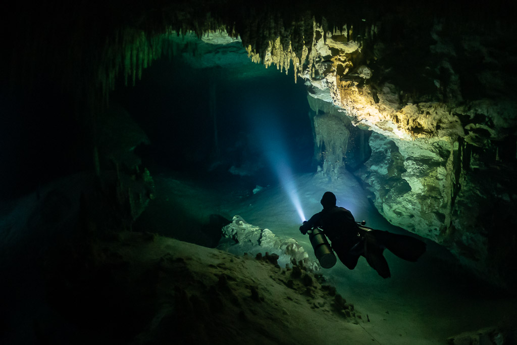 Diver with torch below a high stalactite ceiling in a dark cave, Quintana Roo, Mexico