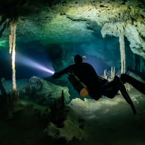 Sidemount diver close to the camera lighting columns in a cave room, Quintana Roo, Mexico