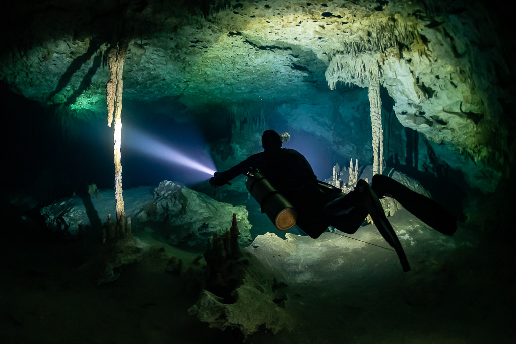 Sidemount diver close to the camera lighting columns in a cave room, Quintana Roo, Mexico