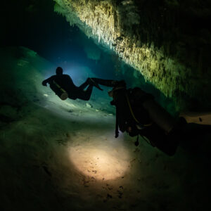 Two divers in a wide low cave, one lighting the sandy floor, Quintana Roo, Mexico