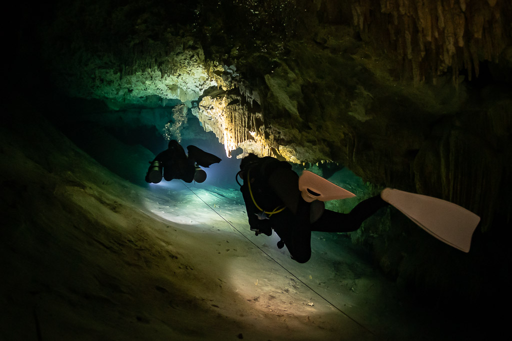 Two divers on a slope in a cave, white fins in the foreground, Quintana Roo, Mexico