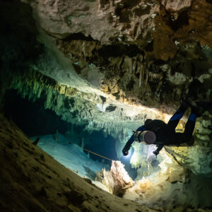 Diver descending a sloping cave passage under a decorated ceiling, Quintana Roo, Mexico