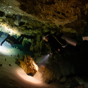 Two divers passing an orange rock block on a pale cave floor, Quintana Roo, Mexico