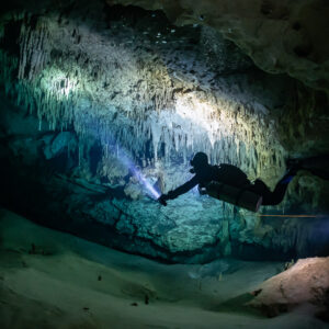 Sidemount diver lighting curtains of stalactites along the guideline, Quintana Roo, Mexico