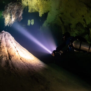 Sidemount diver lighting a large debris cone under a cave ceiling, Quintana Roo, Mexico