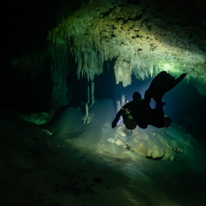 Diver in silhouette entering a stalactite-framed cave passage, Quintana Roo, Mexico
