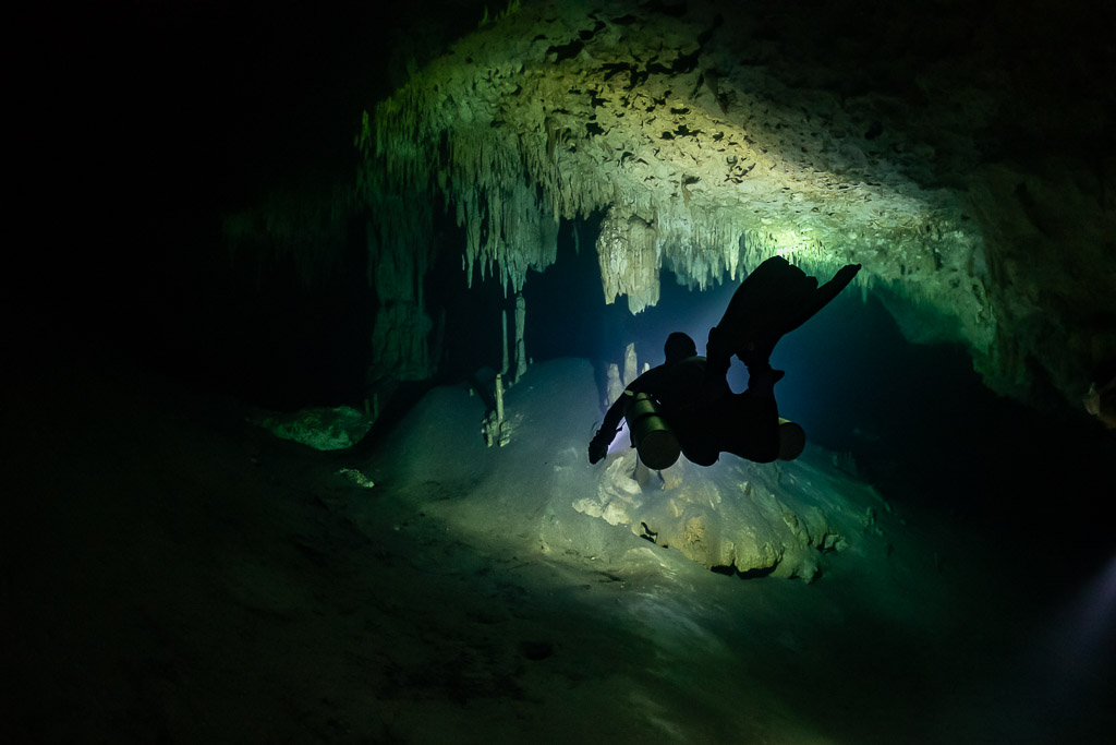 Diver in silhouette entering a stalactite-framed cave passage, Quintana Roo, Mexico