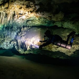 Sidemount diver with blue hood lighting a richly decorated cave wall, Quintana Roo, Mexico