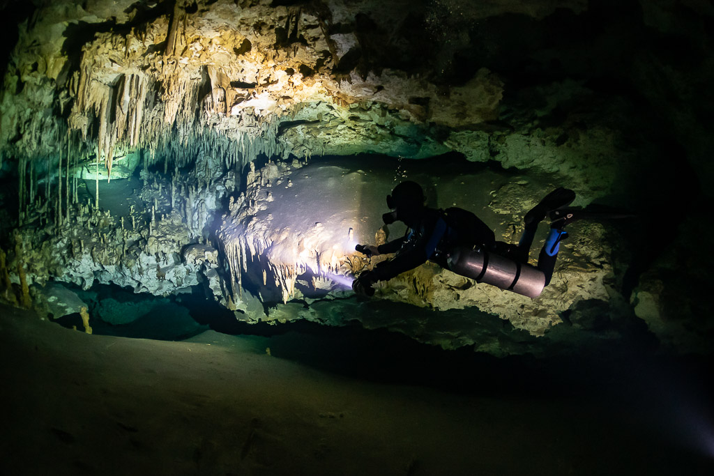 Sidemount diver with blue hood lighting a richly decorated cave wall, Quintana Roo, Mexico
