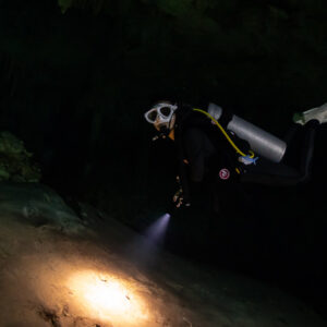 Cavern diver in white mask swimming toward the camera with torch, Quintana Roo, Mexico