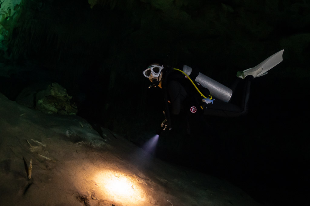Cavern diver in white mask swimming toward the camera with torch, Quintana Roo, Mexico