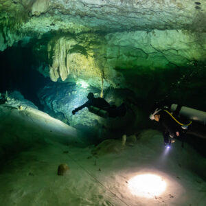 Two divers on a wide sandy cave floor, torch spot in the foreground, Quintana Roo, Mexico