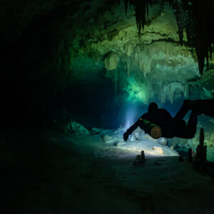 Sidemount diver in silhouette among small stalagmites, green glow behind, Quintana Roo, Mexico