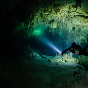 Sidemount diver beaming a torch into a green-lit cave room, Quintana Roo, Mexico