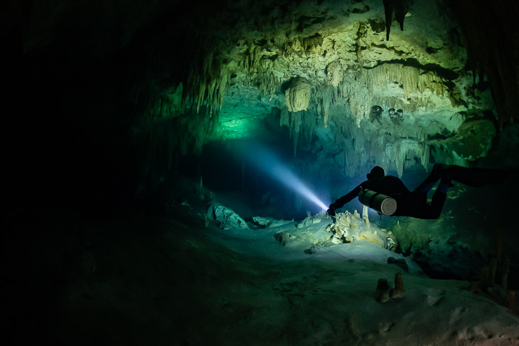 Sidemount diver beaming a torch into a green-lit cave room, Quintana Roo, Mexico