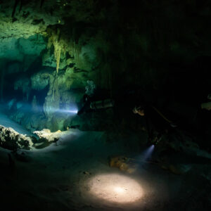 Two divers far apart lighting a wide cave room and its floor, Quintana Roo, Mexico