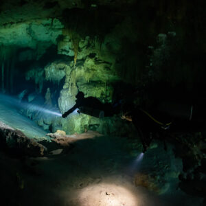 Two divers crossing a wide cave room, torch beams on the sand, Quintana Roo, Mexico