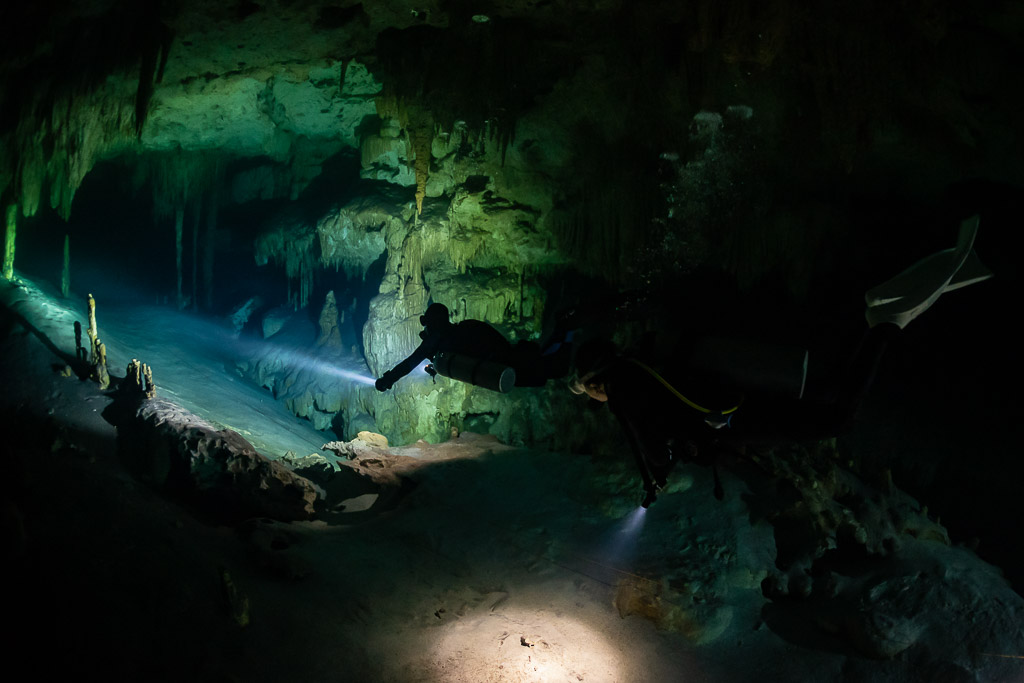 Two divers crossing a wide cave room, torch beams on the sand, Quintana Roo, Mexico