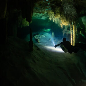 Diver lighting a passage between stalactites in a dark cave, Quintana Roo, Mexico