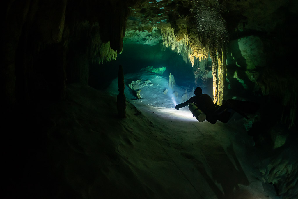 Diver lighting a passage between stalactites in a dark cave, Quintana Roo, Mexico