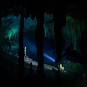 Dark stalactite columns framing a distant torch beam in a cave, Quintana Roo, Mexico