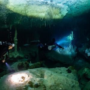 Two divers lighting rocks under the bright surface of a cenote, Quintana Roo, Mexico