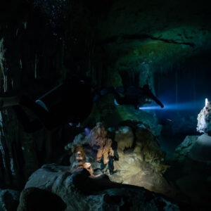 Two divers with torches among boulders in a dark cavern, Quintana Roo, Mexico