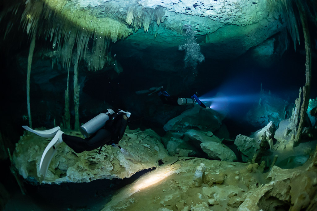 Two divers lighting a passage among columns under the cavern ceiling, Quintana Roo, Mexico