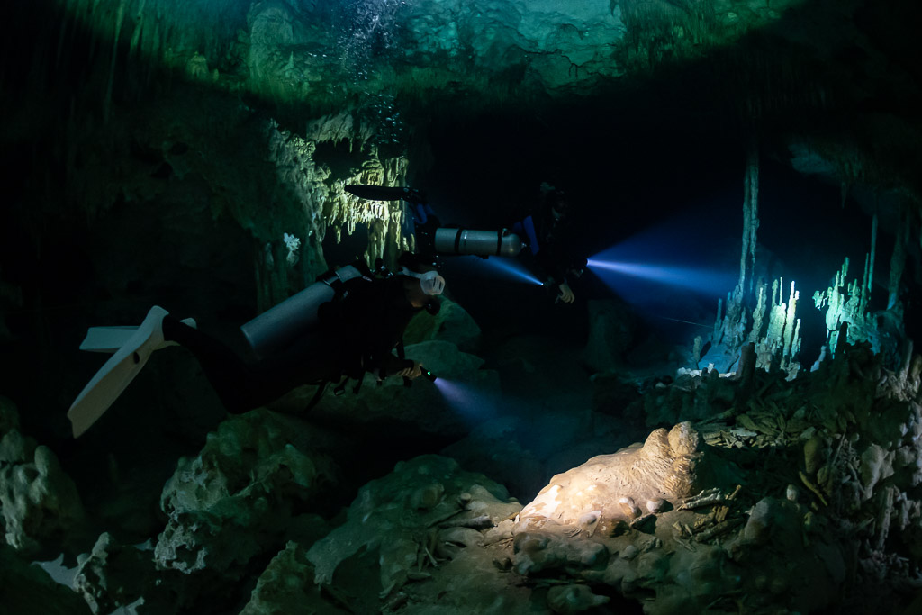 Two divers with torches pointing at white stalactites in a cavern, Quintana Roo, Mexico