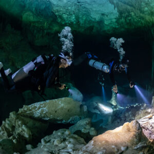 Two divers with bubbles rising, torches lighting rocks below, Quintana Roo, Mexico