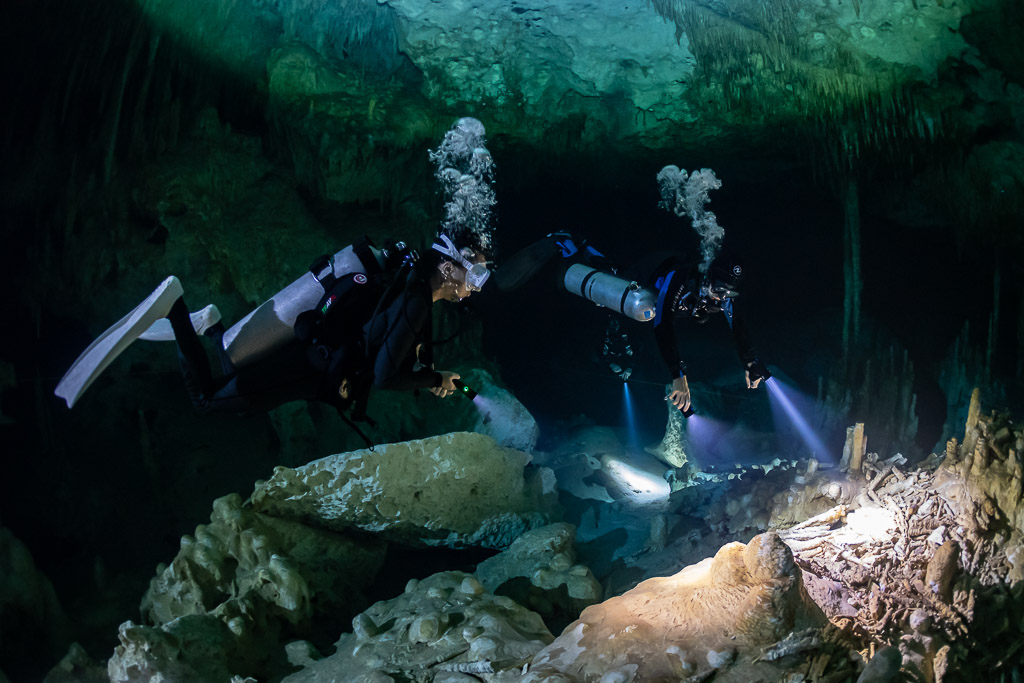 Two divers with bubbles rising, torches lighting rocks below, Quintana Roo, Mexico
