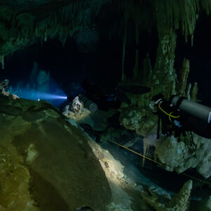 Diver with yellow hose passing a large boulder, second diver beyond, Quintana Roo, Mexico