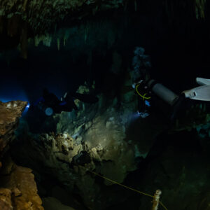 Diver with white fins over a rocky floor lighting toward a blue opening, Quintana Roo, Mexico