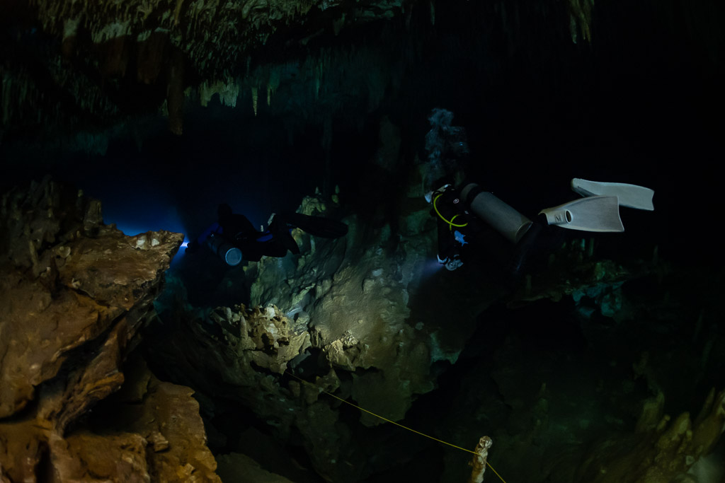 Diver with white fins over a rocky floor lighting toward a blue opening, Quintana Roo, Mexico