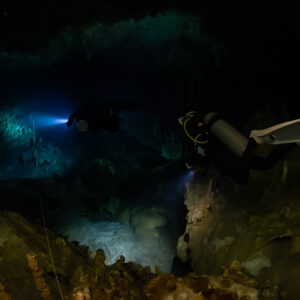 Diver in the dark lighting a pale cave floor beyond orange rocks, Quintana Roo, Mexico