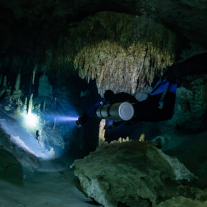 Sidemount diver with blue fins lighting a passage under a stalactite cluster, Quintana Roo, Mexico