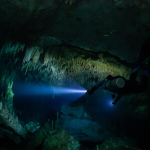 Sidemount diver beaming a blue torch under a stalactite ledge, Quintana Roo, Mexico