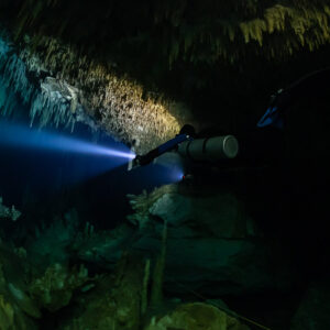 Sidemount diver lighting stalactite curtains, close side view, Quintana Roo, Mexico