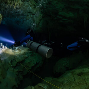 Sidemount diver beside a thin column on a lit rocky floor, Quintana Roo, Mexico