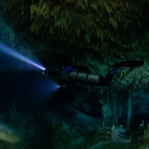 Sidemount diver beaming a long blue torch into the dark, Quintana Roo, Mexico
