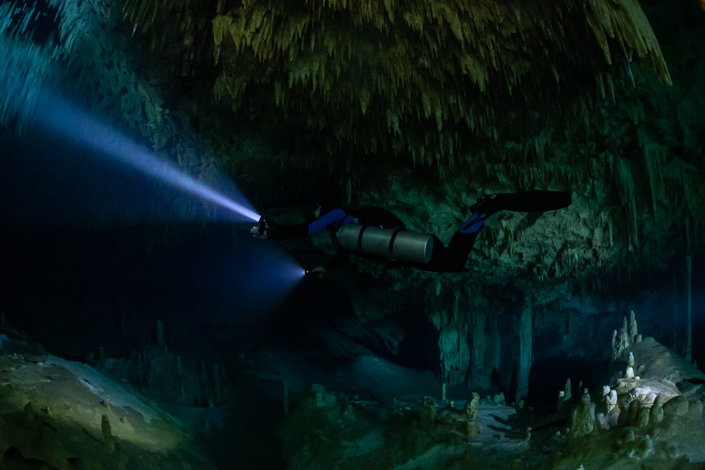 Sidemount diver beaming a long blue torch into the dark, Quintana Roo, Mexico